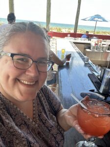 Picture of Kendie sitting at the bar at Joe's Crab Shack in Jacksonville, Florida, on a solo trip to the beach. Kendie is smiling and holding up a goblet containing a red beverage with a straw.